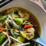 this is a picture of dumpling soup garnished with fresh bean sprouts, jalapeños, and chili crisp