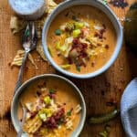 this is a picture of cheeseburger soup garnished with potato chips, bacon bits, and diced dill pickles