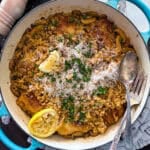 this is an upclose picture of chicken and couscous in a large skillet garnished with lemon, parsley, and flakey sea salt on a dark wooden background