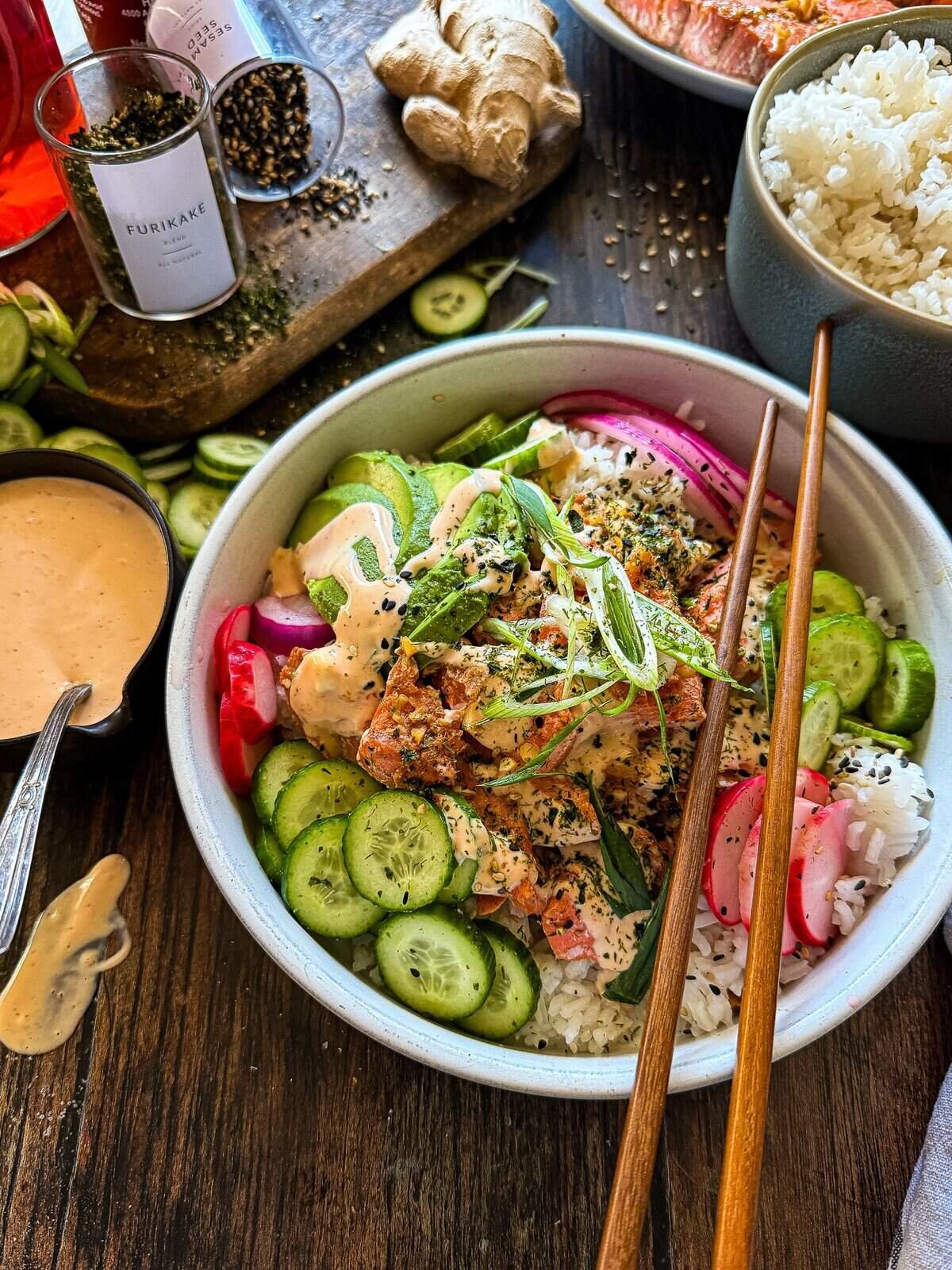 this is a picture of a sushi bowls with pickled onions and radish, salmon, avocado and a green onion garnish with a side of spicy sriracho mayo