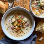 bowl of seafood chowder on a wooden background with a gray napkin and crusty bread
