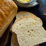 this is a picture of sliced white sandwich bread on a dark surface with a knife and butter to the side