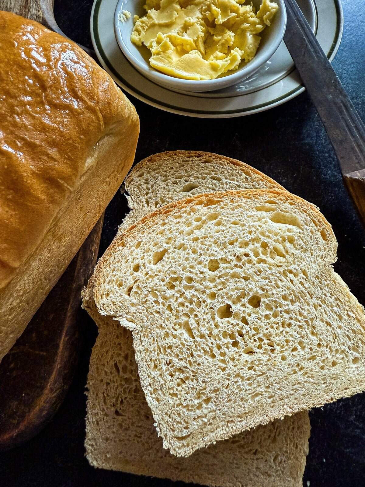 this is a picture of sliced white sandwich bread on a dark surface with a knife and butter to the side
