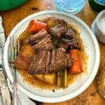 Dutch oven pot roast with vegetables on a rustic wooden table, served on a white plate