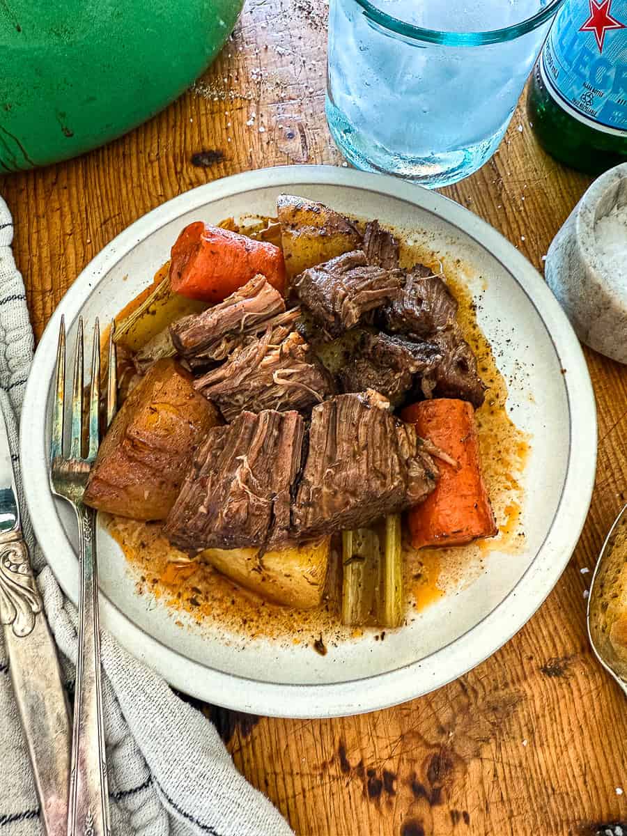 Savory pot roast with vegetables on a rustic wooden table, served on a white plate.