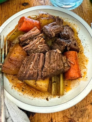 shredded pot roast with potatoes, carrots, celery drizzled with the braising liquid on a white plate