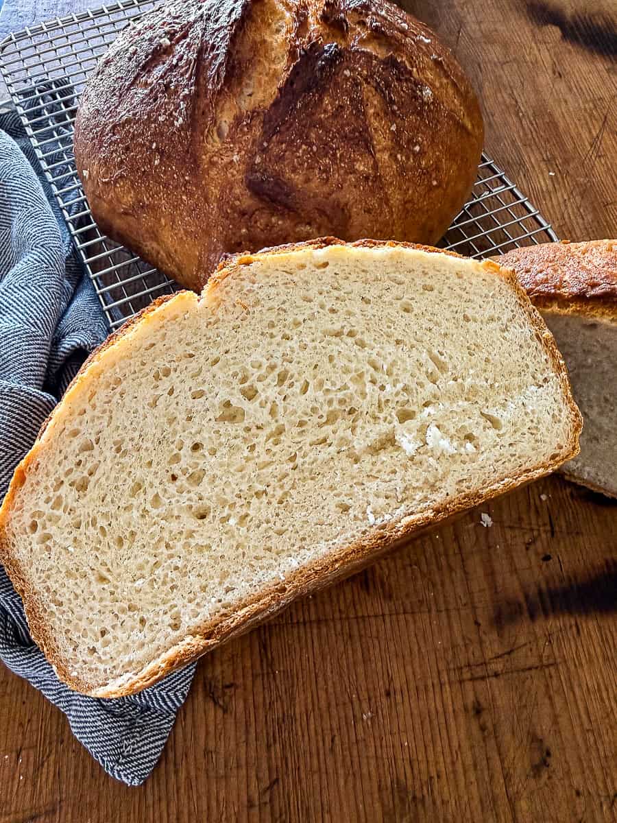 Slice of gluten-free no-knead bread resting on a wire baking rack on a wooden surface next to a dish towel