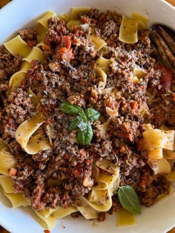 bowl of creamy bolognese tossed with pappardelle pasta and garnished with basil leaves