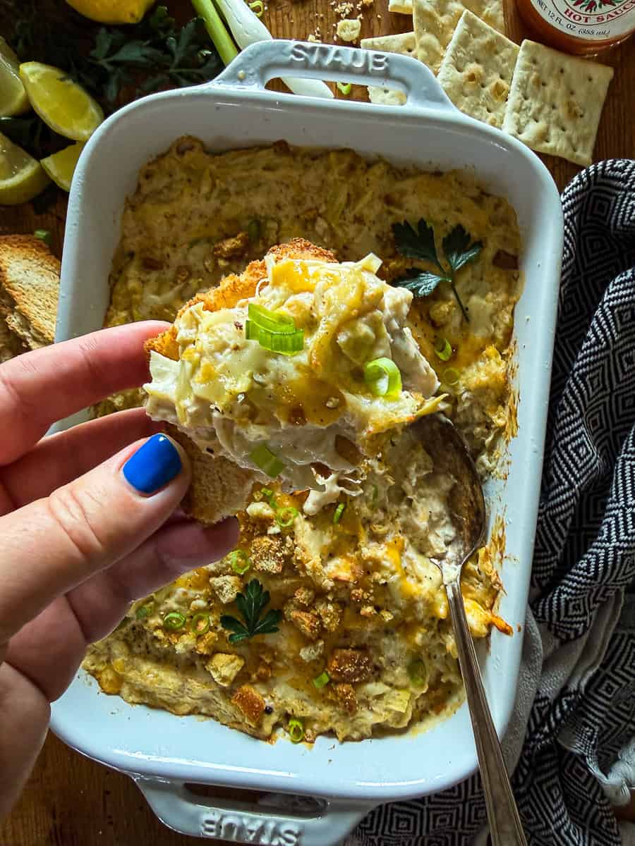 scoop of crab and artichoke dip on a crostini with toasted breadcrumbs and fresh herb garnish