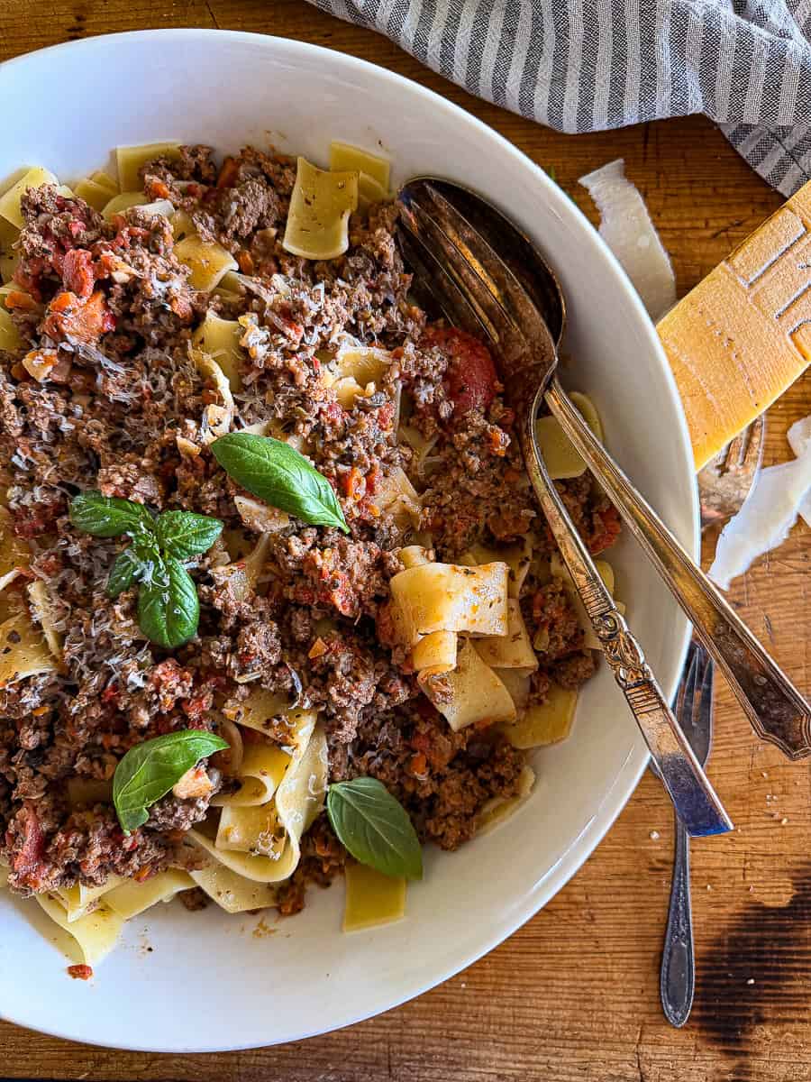 bowl of creamy bolognese tossed with pappardelle pasta and garnished with basil leaves