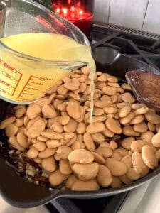 chicken broth being poured into a skillet of butter beans