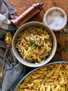 cafeteria noodles garnished with fresh chives in a gray bowl on a wooden surface