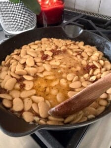 a wooden spoon smashing butter beans in a cast iron skillet