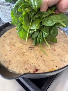 fresh spinach being added to a cast iron skillet of marry me butter beans