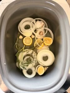 slow cooker loaded with onions, lemons, garlic, and fresh herbs