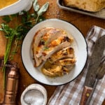 sliced slow cooker turkey breast served on a wooden background garnished with fresh herbs and a container of gravy