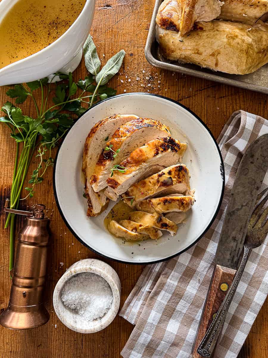 sliced slow cooker turkey breast served on a wooden background garnished with fresh herbs and a container of gravy